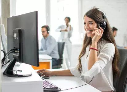 Frau, die vor einem PC sitzt mit einem Headset und telefoniert