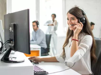 Frau, die vor einem PC sitzt mit einem Headset und telefoniert