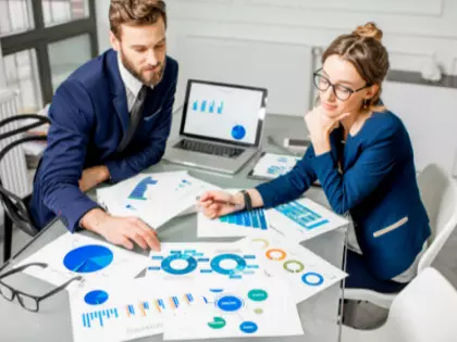 Ein Mann und eine Frau sitzen über diverse Charts gebeugt an einem Tisch