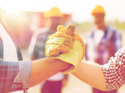 zwei Arme von Arbeitern, die einschlagen, im Hintergrund zwei Bauarbeiter